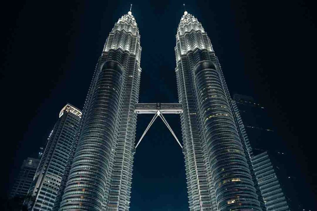 The iconic Petronas Twin Towers in Kuala Lumpur, Malaysia, standing tall against a blue sky with the connecting Skybridge visible between the towers
